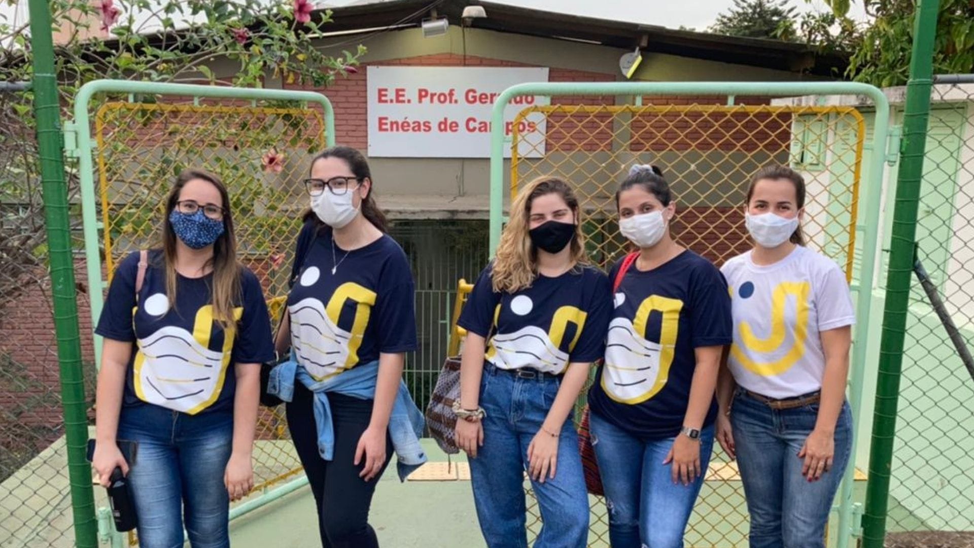 A imagem mostra as quatro alunas responsáveis pelo projeto e a orientadora pedagógica em frente a escola estadual.