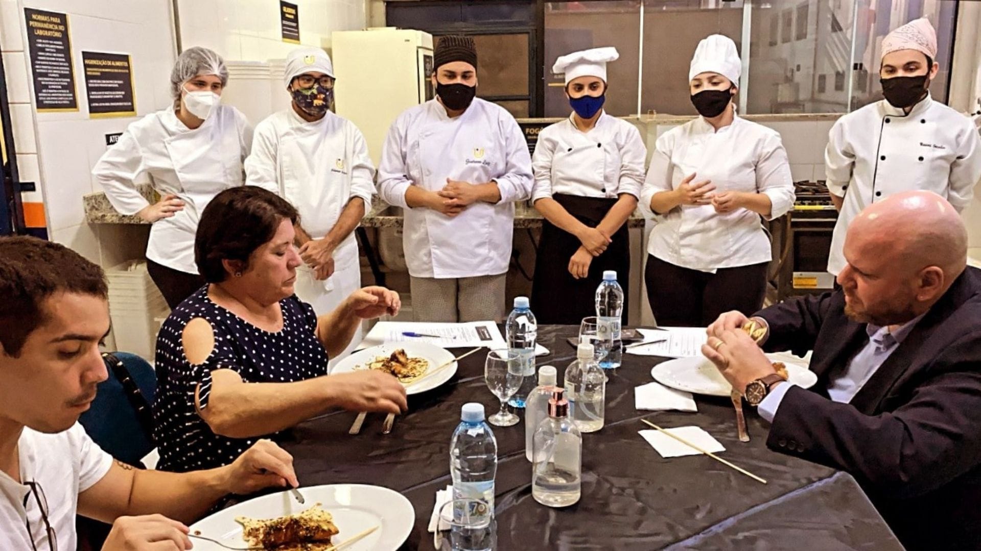 A imagem mostra a bancada avaliadora do Evento Gastronômico Pedagógico provando pratos criados pelos alunos.