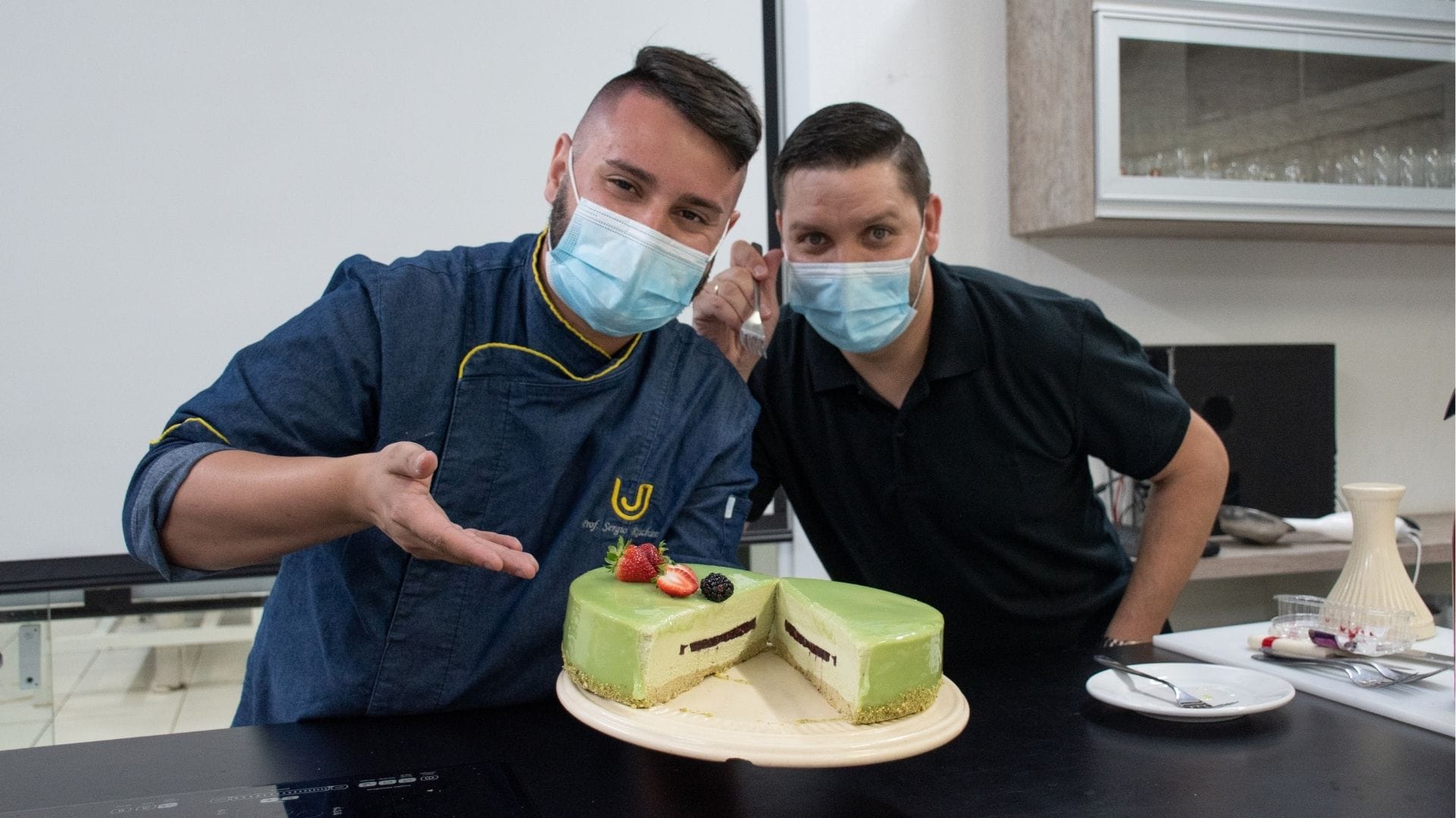 A imagem mostra os professores Sérgio Rischiotto e Tibério Gil preparando um entremèts durante a aula remota.