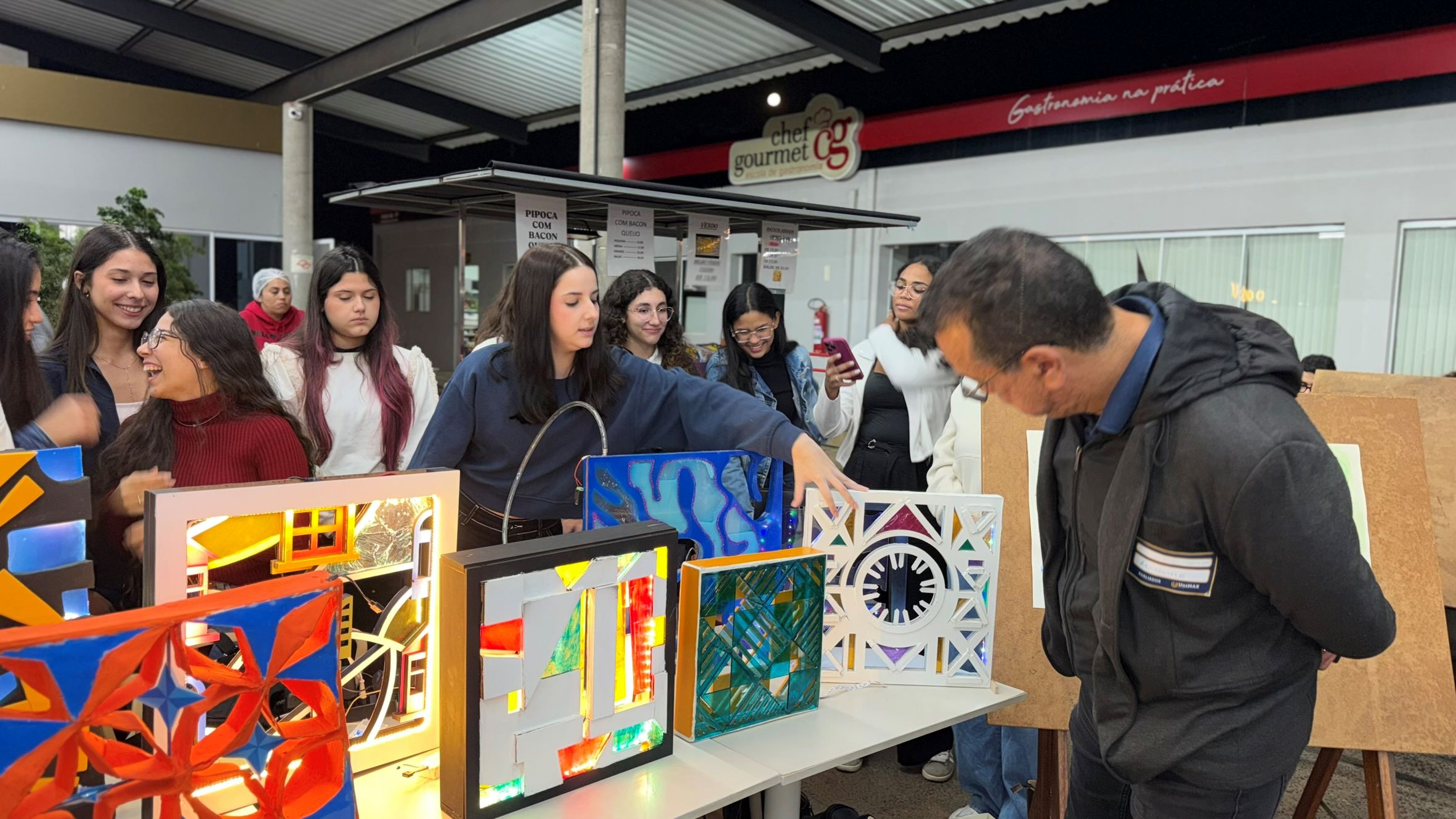 Em diferentes estandes, estudantes apresentam projetos de empreendedorismo e inovação para avaliadores e visitantes. As fotos mostram protótipos, maquetes, telas com apresentações, demonstrações de soluções, conversas entre participantes e bancas de avaliação em um ambiente de exposição acadêmica.